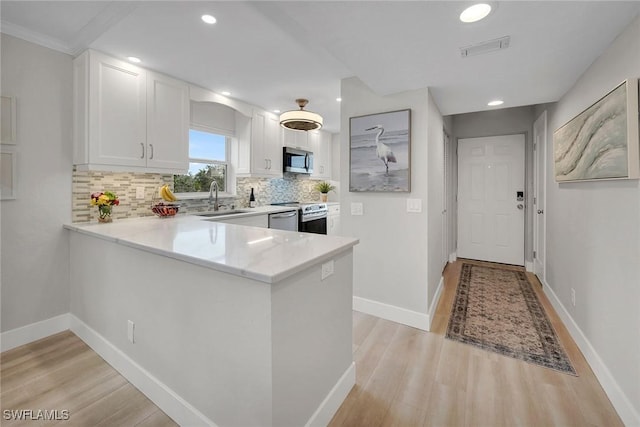 kitchen featuring appliances with stainless steel finishes, white cabinetry, sink, light hardwood / wood-style floors, and kitchen peninsula