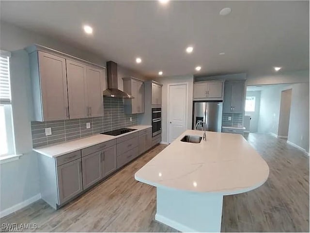 kitchen with sink, gray cabinetry, appliances with stainless steel finishes, an island with sink, and wall chimney range hood