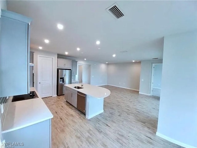 kitchen featuring sink, light wood-type flooring, stainless steel appliances, and a center island with sink