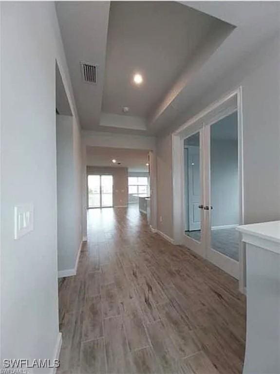 corridor with hardwood / wood-style floors, a raised ceiling, and french doors