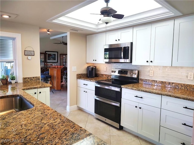 kitchen featuring backsplash, stainless steel appliances, a tray ceiling, white cabinets, and dark stone counters