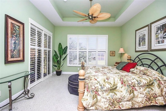 carpeted bedroom featuring ceiling fan and a tray ceiling