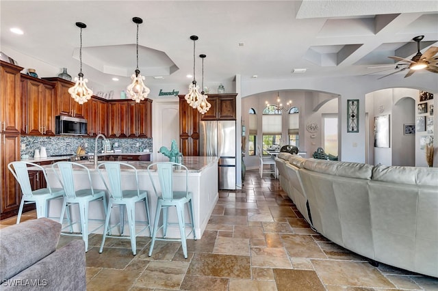 kitchen with a large island, a breakfast bar area, backsplash, stainless steel appliances, and decorative light fixtures