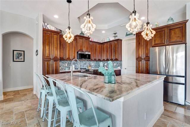 kitchen with appliances with stainless steel finishes, decorative light fixtures, light stone countertops, and a large island with sink