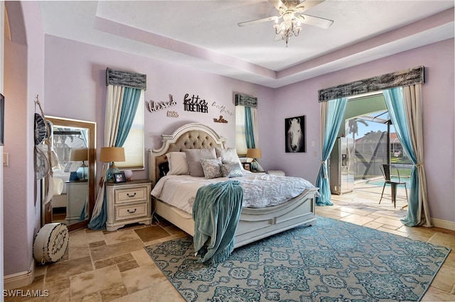 bedroom with ceiling fan, a tray ceiling, and access to exterior