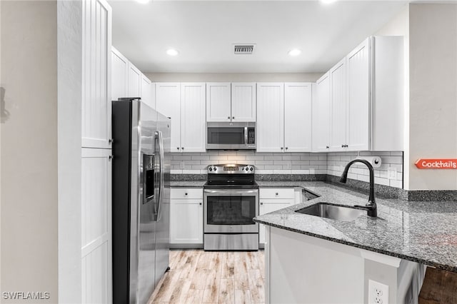 kitchen with sink, appliances with stainless steel finishes, dark stone countertops, light hardwood / wood-style floors, and white cabinets