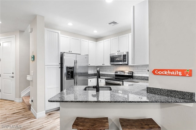 kitchen with a breakfast bar area, white cabinetry, stainless steel appliances, kitchen peninsula, and dark stone counters