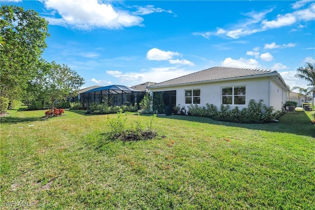 rear view of house featuring glass enclosure, a tile roof, a lawn, and stucco siding