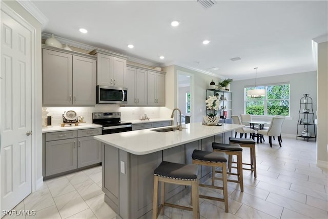 kitchen featuring gray cabinets, light countertops, appliances with stainless steel finishes, a sink, and an island with sink