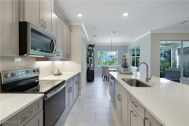 kitchen featuring appliances with stainless steel finishes, hanging light fixtures, a sink, crown molding, and backsplash