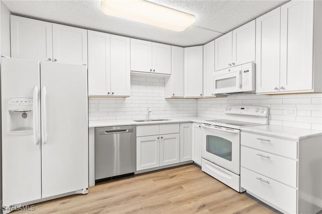 kitchen with sink, white appliances, light hardwood / wood-style flooring, white cabinetry, and backsplash