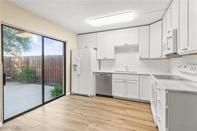 kitchen with white cabinetry, sink, light wood-type flooring, backsplash, and white appliances