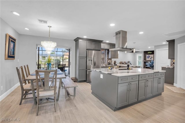 kitchen featuring a kitchen island with sink, stainless steel fridge, gray cabinetry, and island exhaust hood