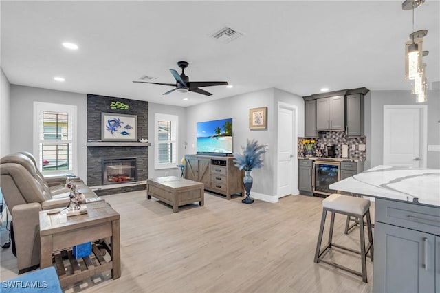 living room featuring a healthy amount of sunlight, beverage cooler, a fireplace, and light hardwood / wood-style flooring