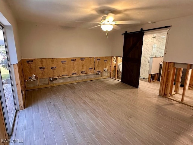 unfurnished room with a barn door, ceiling fan, and light hardwood / wood-style flooring