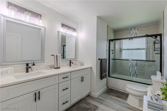 full bathroom featuring double vanity, bath / shower combo with glass door, a sink, and toilet