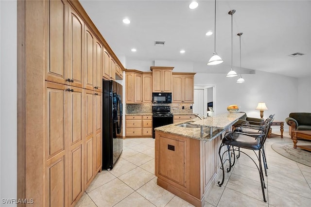 kitchen with decorative light fixtures, a breakfast bar area, light stone counters, black appliances, and a center island with sink