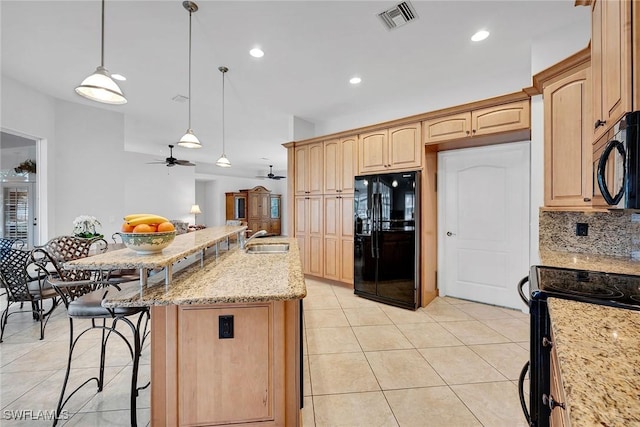 kitchen with sink, light stone counters, hanging light fixtures, a kitchen island with sink, and black appliances