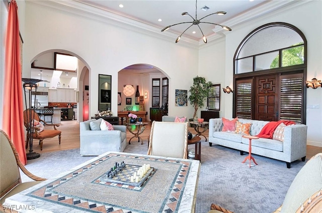 living room with hardwood / wood-style floors, crown molding, a chandelier, and a towering ceiling