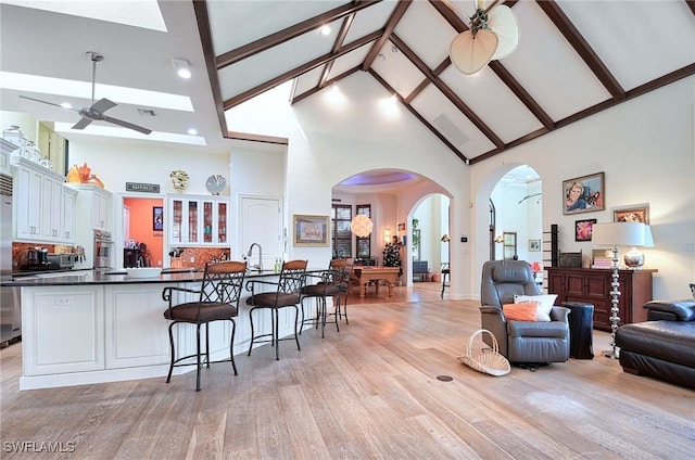 interior space with ceiling fan, a kitchen breakfast bar, white cabinets, oven, and light wood-type flooring