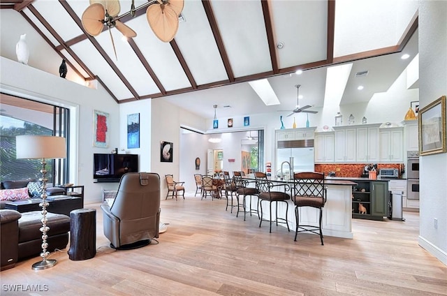 interior space with a breakfast bar, light hardwood / wood-style flooring, appliances with stainless steel finishes, ceiling fan, and a kitchen island with sink