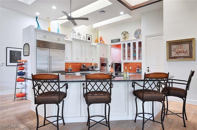 kitchen with white cabinetry, a kitchen breakfast bar, kitchen peninsula, and stainless steel built in refrigerator