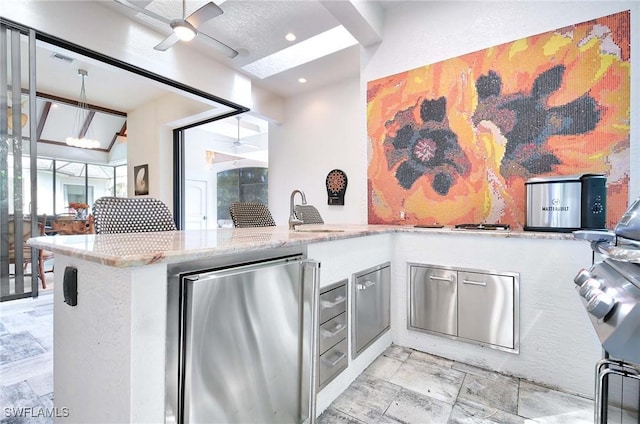 kitchen featuring sink, fridge, kitchen peninsula, ceiling fan, and light stone countertops