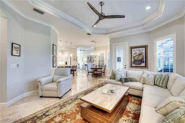 living room featuring a tray ceiling, plenty of natural light, ornamental molding, and ceiling fan with notable chandelier