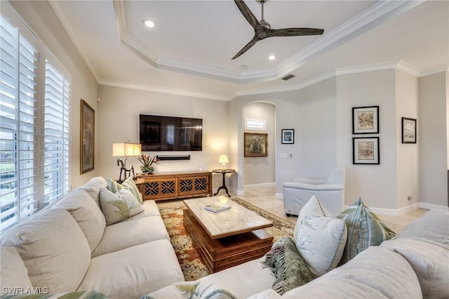 living room featuring a raised ceiling, ornamental molding, a healthy amount of sunlight, and ceiling fan