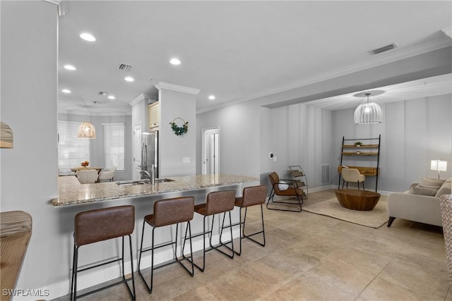 kitchen with ornamental molding, freestanding refrigerator, a breakfast bar area, light stone counters, and recessed lighting