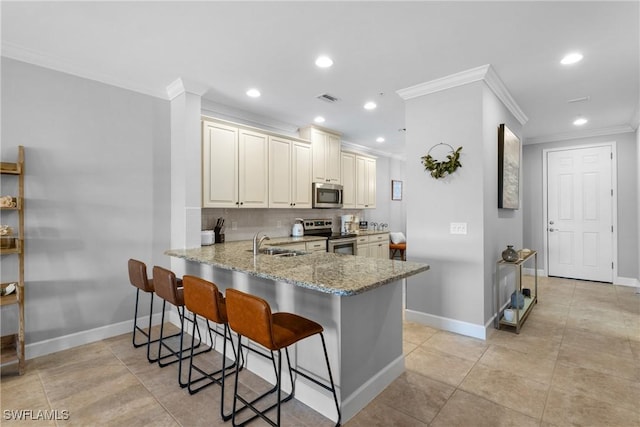 kitchen with appliances with stainless steel finishes, ornamental molding, a sink, light stone counters, and a kitchen bar