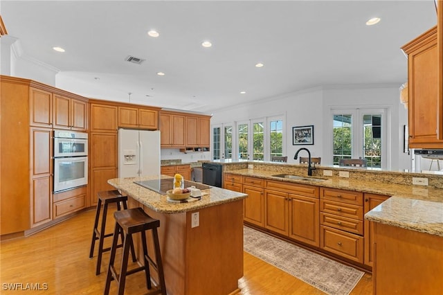 kitchen with sink, a kitchen bar, a kitchen island with sink, black appliances, and light stone countertops