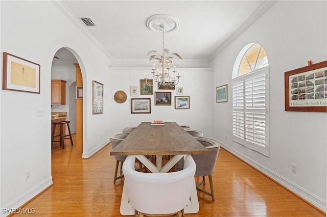 dining room featuring light wood finished floors, visible vents, arched walkways, and crown molding