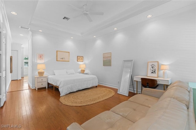 bedroom with a raised ceiling, wood finished floors, visible vents, and recessed lighting