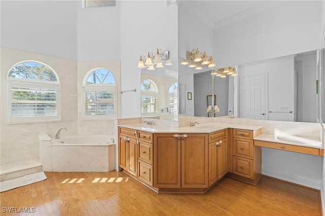 full bathroom with double vanity, ornamental molding, wood finished floors, a sink, and a bath