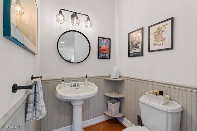 half bathroom with a wainscoted wall, wood finished floors, and toilet