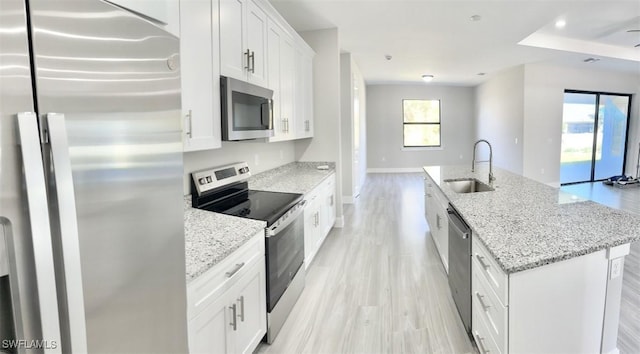 kitchen with sink, appliances with stainless steel finishes, a kitchen island with sink, light stone counters, and white cabinets