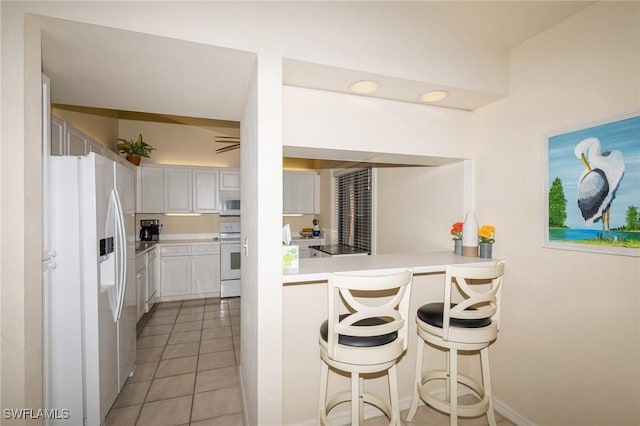 kitchen featuring white cabinetry, light tile patterned floors, a kitchen breakfast bar, kitchen peninsula, and white appliances