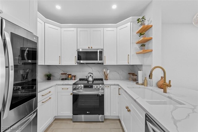 kitchen featuring light tile patterned floors, stainless steel appliances, a sink, white cabinets, and decorative backsplash