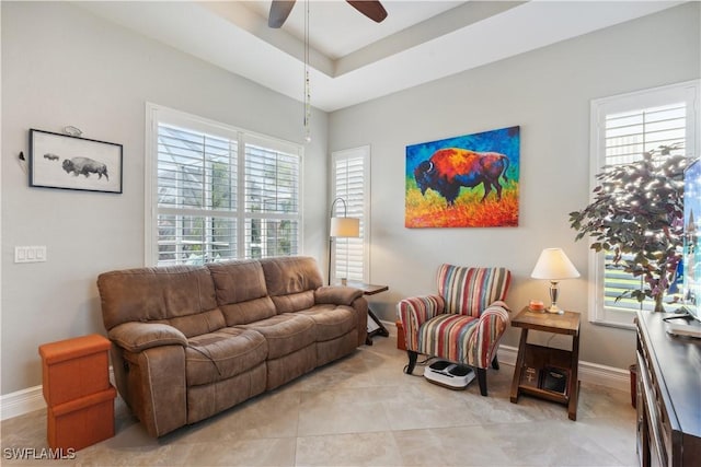 living room featuring light tile patterned flooring, ceiling fan, and a tray ceiling