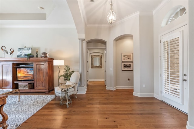 entrance foyer featuring ornamental molding, a chandelier, hardwood / wood-style floors, and ornate columns