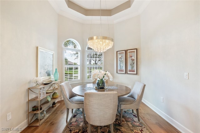 dining space with hardwood / wood-style floors, a notable chandelier, a raised ceiling, and a high ceiling