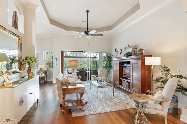 living area with dark wood-type flooring, a raised ceiling, ceiling fan, and a high ceiling