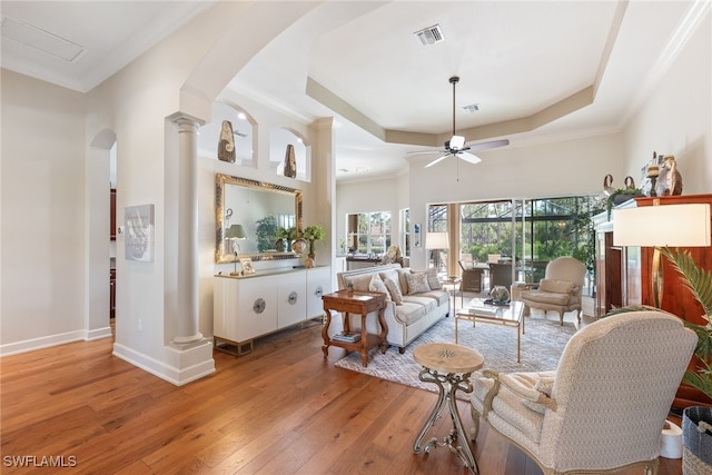 living room with hardwood / wood-style flooring, ornamental molding, decorative columns, and a raised ceiling