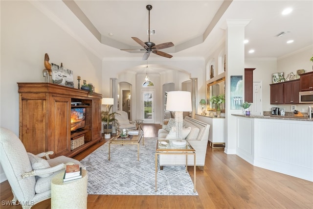 living room with crown molding, ceiling fan, a tray ceiling, and light hardwood / wood-style floors