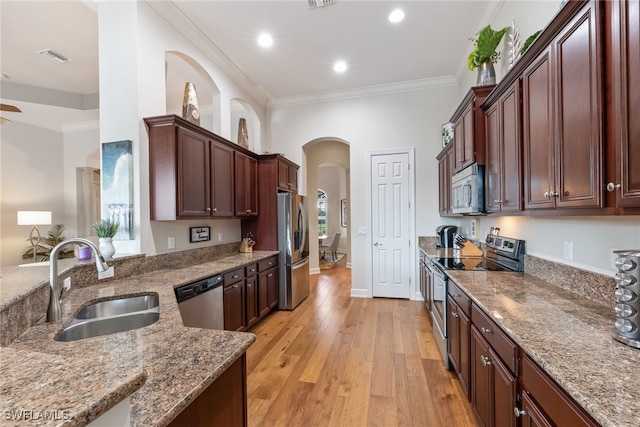 kitchen featuring sink, appliances with stainless steel finishes, ornamental molding, light hardwood / wood-style floors, and dark stone counters