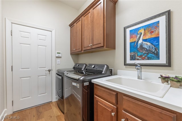 laundry area featuring cabinets, washing machine and dryer, sink, and light hardwood / wood-style floors