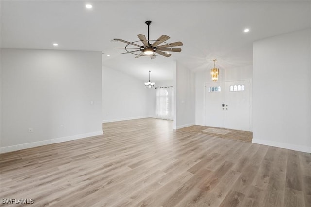 unfurnished living room featuring lofted ceiling, ceiling fan with notable chandelier, light wood-type flooring, and baseboards