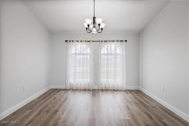 spare room featuring baseboards, wood finished floors, and an inviting chandelier