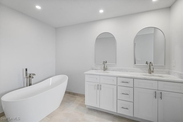 full bath featuring a freestanding bath, double vanity, a sink, and recessed lighting